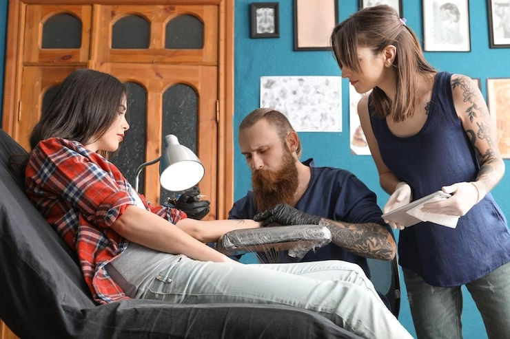 woman getting a tattoo in a studio with a tattoo artist and an assistant
